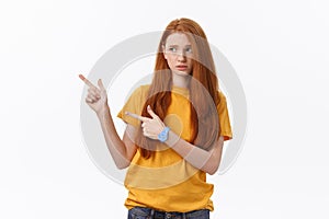 Portrait of happy young woman standing isolated over white wall background. Looking camera showing copyspace pointing