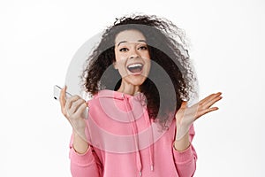 Portrait of happy young woman use smartphone, rejoicing and shouting from joy, winning money on mobile phone, triumphing