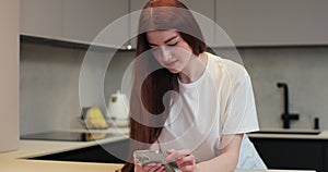 Portrait of happy young woman using smartphone in the home kitchen. Woman choosing recipe on mobile phone. Lifestyle and