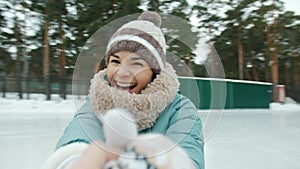 Portrait of happy young woman in warm clothes ice-skating laughing looking at camera