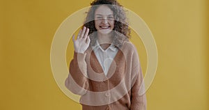 Portrait of happy young woman waving hand and smiling looking at camera greeting people