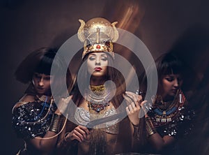 Portrait of haughty Egyptian queen in an ancient pharaoh costume with two concubines.