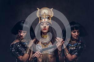 Portrait of haughty Egyptian queen in an ancient pharaoh costume with two concubines.