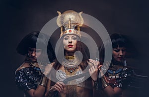 Portrait of haughty Egyptian queen in an ancient pharaoh costume with two concubines.