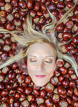 Portrait, head of young beauty caucasian woman with blonde hair and closed eye in chestnut background. Autumn, cosmetics concept