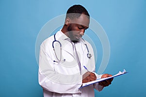 Portrait of health care medic in white lab coat holding clipboard writing on patient chart