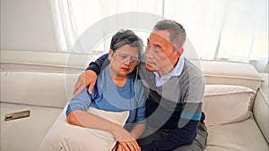Portrait of healthy senior man and woman embracing and sitting on sofa at home, Happy senior married couple spending