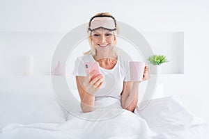 Portrait of her she nice attractive cheerful cheery senior woman drinking beverage sitting in bed sending sms chatting
