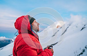 Portrait of high altitude mountaineer dressed red warm dawn jacket holding metal mug of hot tea thinking and enjoying fresh