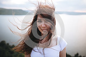 Portrait of hipster girl with windy hair standing on top of rock mountain with beautiful sunset view on river. Atmospheric