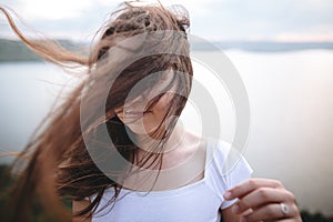 Portrait of hipster girl with windy hair standing on top of rock mountain with beautiful sunset view on river. Atmospheric