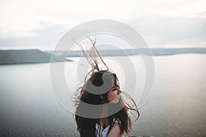 Portrait of hipster girl with windy hair standing on top of rock mountain with beautiful sunset view on river. Atmospheric