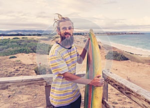 Portrait of Hipster Surfer with dreadlocks and beard looking at the ocean with vintage surfboard