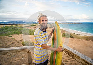 Portrait of Hipster Surfer with dreadlocks and beard looking at the ocean with vintage surfboard