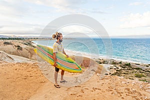 Portrait of Hipster Surfer with dreadlocks and beard looking at the ocean with vintage surfboard