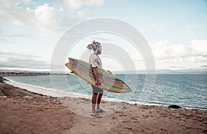 Portrait of Hipster Surfer with dreadlocks and beard looking at the ocean with vintage surfboard