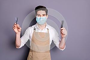 Portrait of his he attractive guy barber wearing safety mask holding in hands scissors comb social distance stop