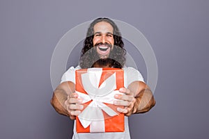 Portrait of his he nice attractive cheerful cheery ecstatic overjoyed wavy-haired guy giving you showing red gift box