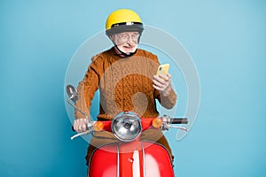 Portrait of his he nice attractive cheerful cheery focused bearded grey-haired man riding moped using gadget chatting