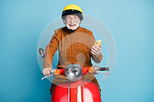 Portrait of his he nice attractive cheerful cheery glad bearded grey-haired man riding moped using device gadget