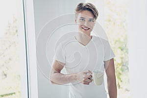 Portrait of his he nice attractive cute cheerful cheery guy drinking early morning sweet hot cacao at light white modern