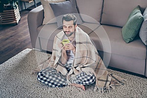 Portrait of his he nice attractive dreamy cheery brunet guy sitting on carpet watching tv drinking cacao homey cosy