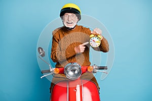 Portrait of his he nice attractive funky cheerful cheery glad bearded grey-haired man riding moped holding in hand clock
