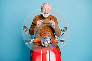 Portrait of his he nice attractive funky cheerful cheery glad delighted bearded grey-haired man riding moped having fun