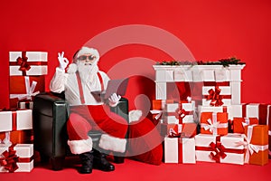 Portrait of his he nice attractive funky fat bearded cheerful Santa using laptop sitting in armchair showing ok-sign