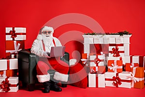 Portrait of his he nice attractive funky fat cheerful Santa using laptop sitting in armchair reading e-mail order shop
