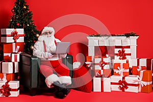 Portrait of his he nice attractive funky fat cheerful Santa using laptop sitting in armchair responding answering e-mail