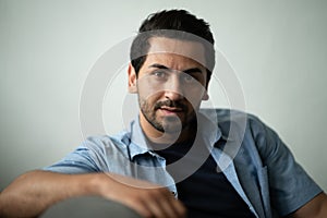 Portrait of Hispanic Arabian handsome beard man looks serious sitting at the armchair while looking toward the camera in the