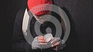 Portrait of homeless beggar in the rain counting change lying in Cup for money