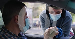 Portrait of homeless woman thanking for cash in slow motion leaning on car window. Man in coronavirus face mask helping