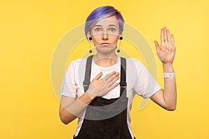 Portrait of honest serious hipster girl swearing with hand on her heart chest, making promise. yellow background, studio shot