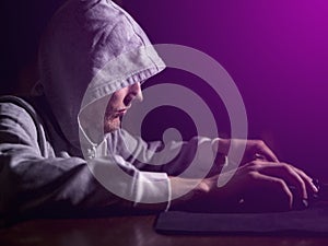 Portrait of hooded man typing text on keyboard in front of pc monitor late in night