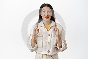 Portrait of hopeful brunette woman cross fingers and looking up with anticipation and hope, making wish, smiling