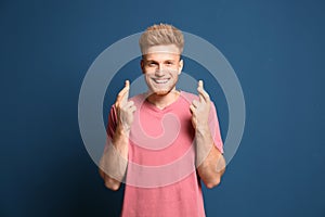 Portrait of hopeful man with crossed fingers on blue