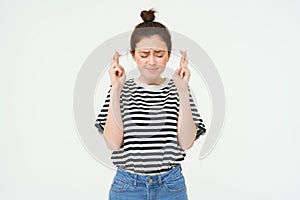 Portrait of hopeful young woman, makes wish, cross fingers for good luck, wishing, anticipating, standing over white