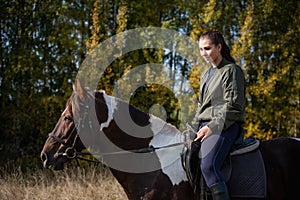 Portrait of a horsewoman in a black leather jacket on a horse against the background of the forest