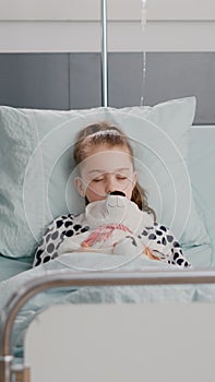 Portrait of hospitalized sick child falling asleep while holding teddy bear in hands