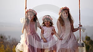 Portrait of hree beautiful little girls swinging on a swing under a big tree.