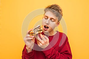 Portrait of a hungry guy looking at an appetizing buggy burger in his hand and going to eat. A very hungry young man eats a burger