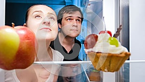 Portrait of hungry man and woman looking for something to eat in fridge at night