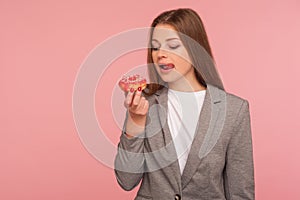 Portrait of hungry woman, office worker in business suit looking at sweet doughnut with desire