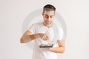 Portrait of hungry young man eating fresh tasty sushi rolls with chopsticks on white isolated background.