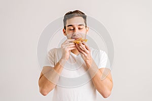 Portrait of hungry young man with enjoying bitting delicious slice of pizza, with closed eyes from pleasure on white