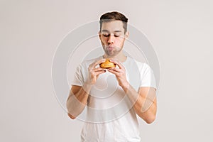Portrait of hungry young man with enjoying eating delicious burger on white isolated background.