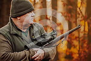 Portrait of hunter or ranger with gun or rifle in the forest looking out or hunting of some venison, hunting period