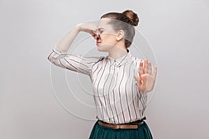 Portrait of ignoring beautiful young woman in striped shirt with makeup and collected ban hairstyle, standing with stop gesture